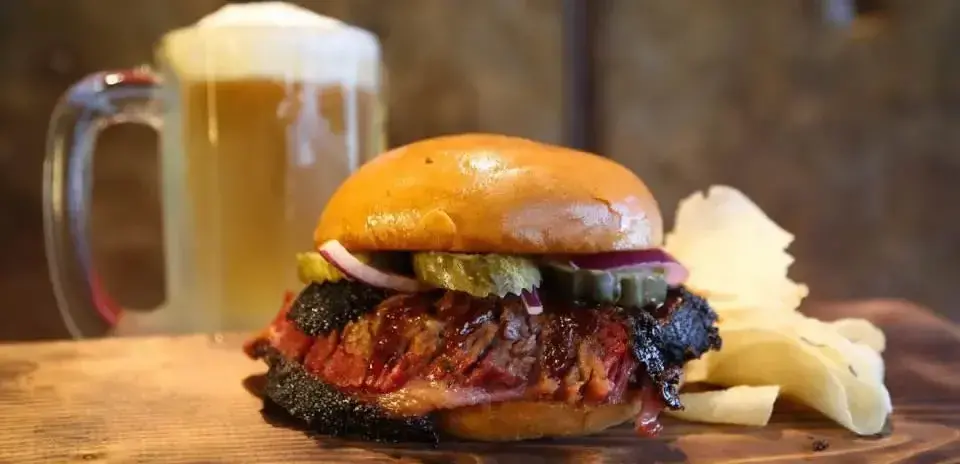 A burguer with onion, chips and a jar of beer
